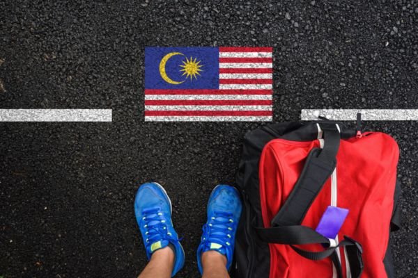 A malysia flag on the road with red bag beside the human foot who wear blue colors flag who wants to study abroad through the best Overseas Education Consultants in Saudi Arabia.